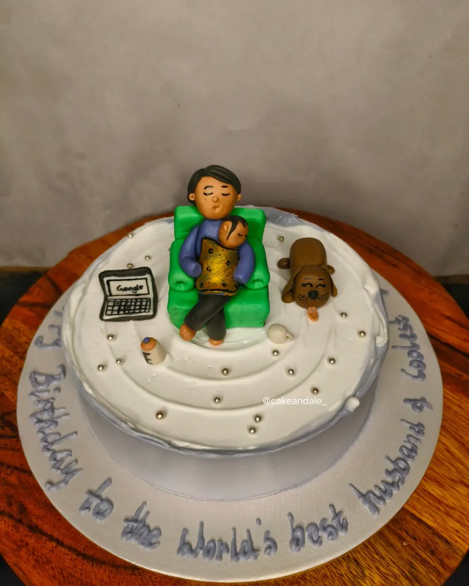 White birthday cake with a fondant dad napping with his baby, a laptop and a sleepy puppy