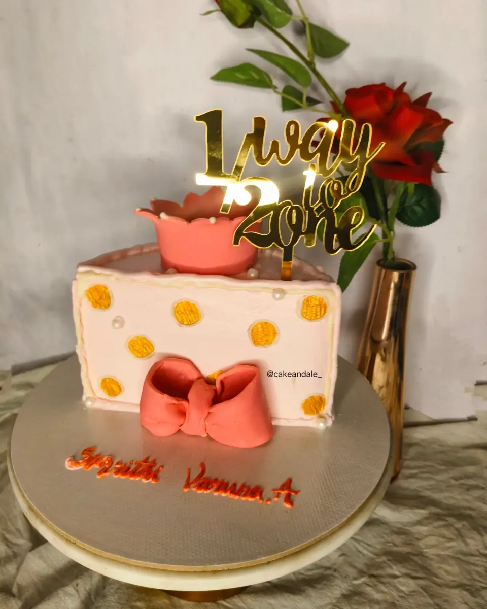 Half cake shaped like a slice with a crown, coral bow and gold "1/2 way to 2" topper