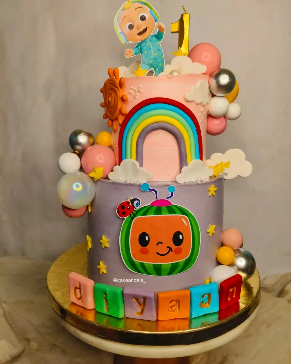 Two tier Cocomelon birthday cake with a fondant rainbow, pastel balls and name blocks